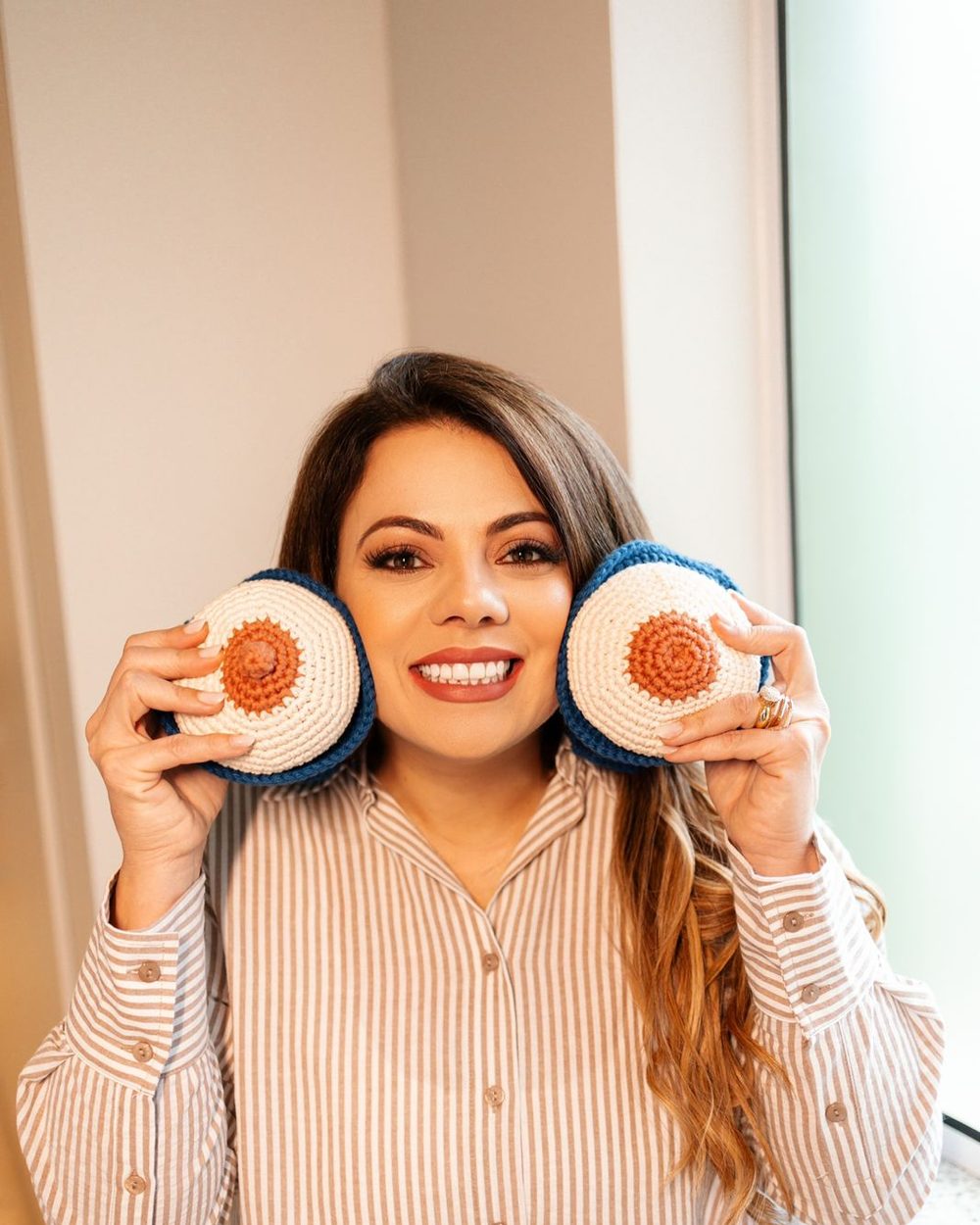 Daniela Camerieri, fonoaudióloga IBCLC, segurando modelos de mama em crochê usados no ensino de amamentação